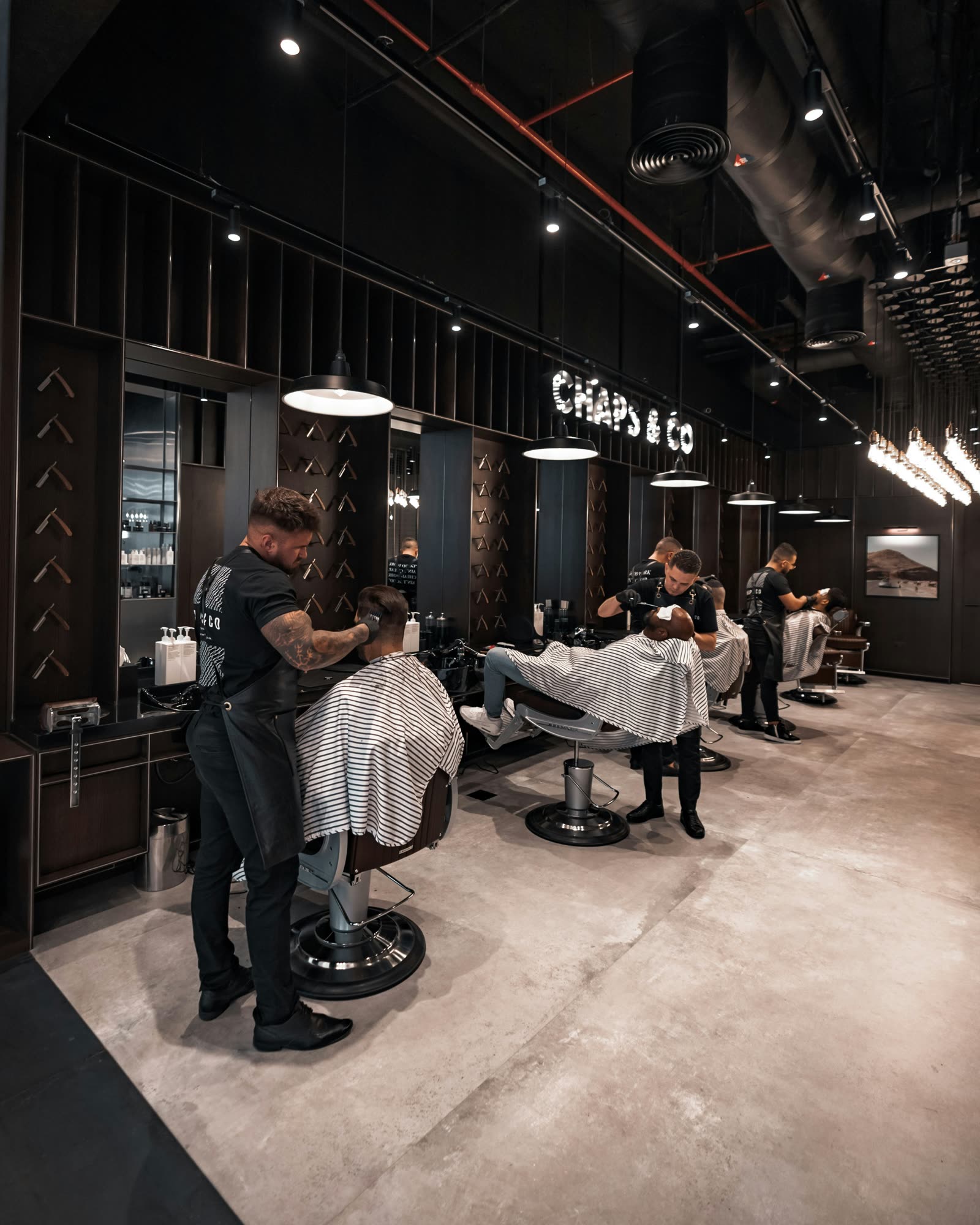 The Fade & Co. floor — black walls, concrete and a row of chairs